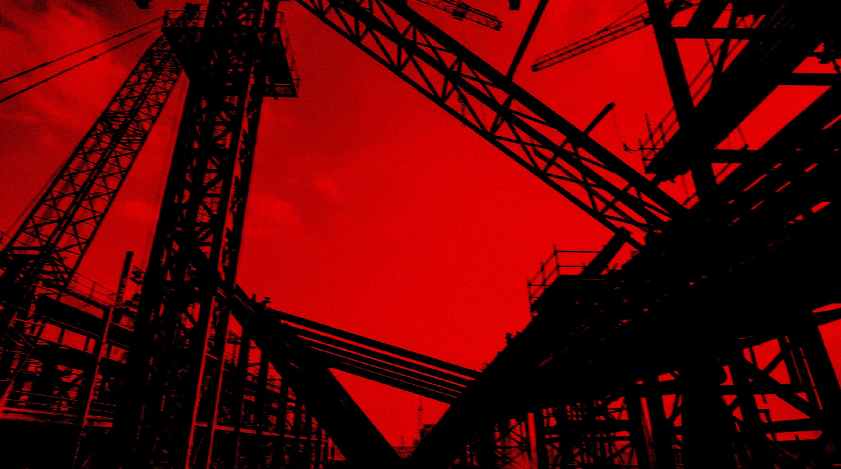 Red and black silhouette of construction cranes against a red sky